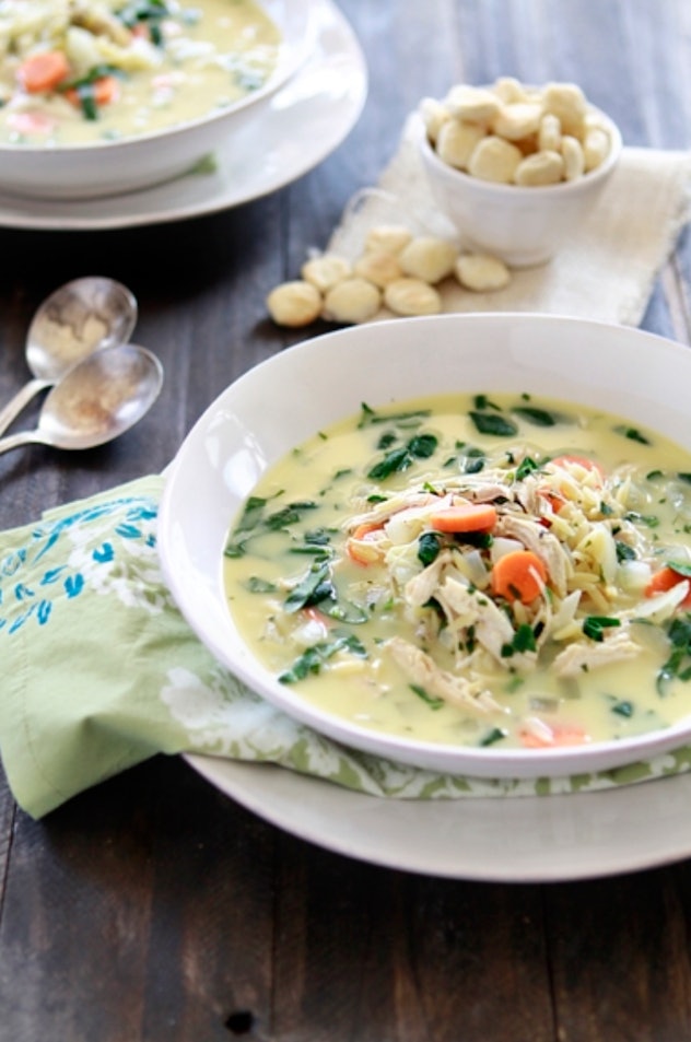 Instant pot lemon chicken spinach and orzo soup in a white bowl with oyster crackers in the backgrou...