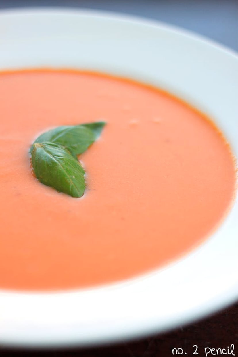 close up of slow cooker tomato soup in white bowl with green garnish