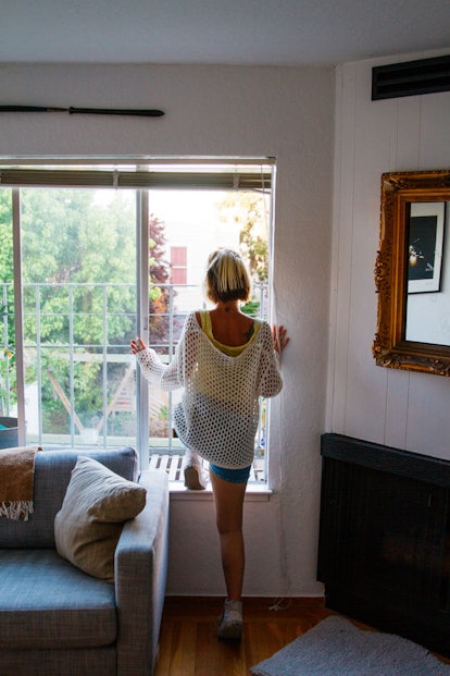 A woman with blonde, short hair is standing in the window of a cozy apartment.