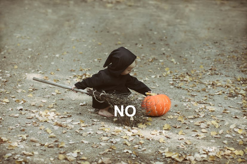 Small child in witch costume plays with broom and pumpkin.