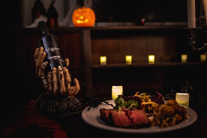 A dinner entree from Refinery's Hotel of Horrors room service menu sits on a table next to a bottle ...
