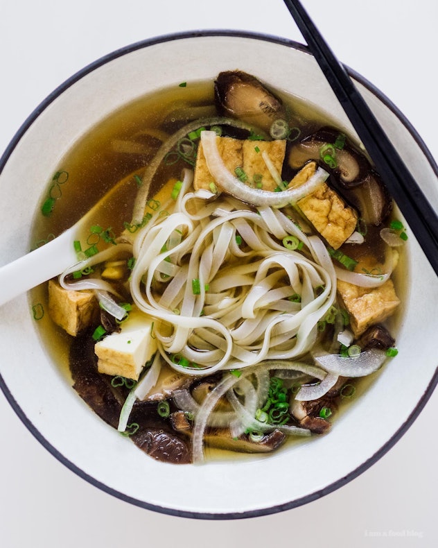 A white bowl of vegan pho sits on a white background. 