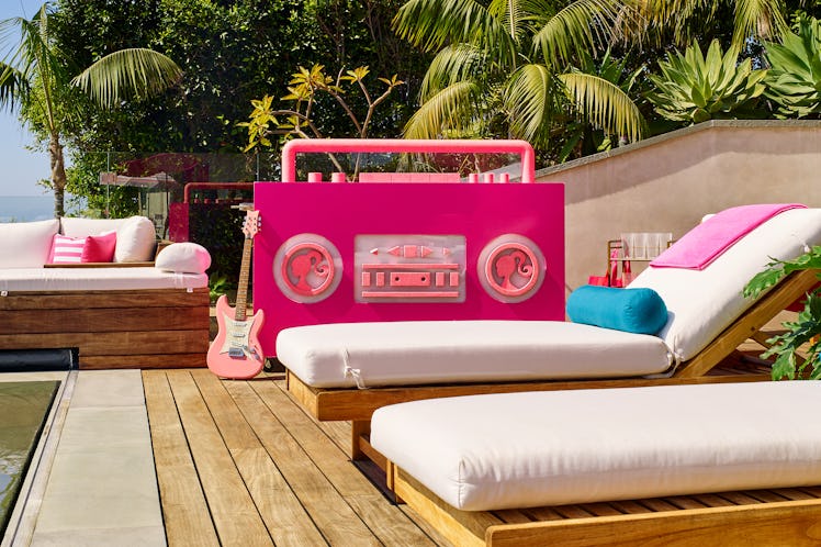 The outdoor deck at Barbie's Malibu Dreamhouse has wooden lounge chairs with white cushions, a giant...