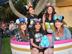 A group of friends wearing Minnie ears are sitting in a teacup spending a day at Disneyland.