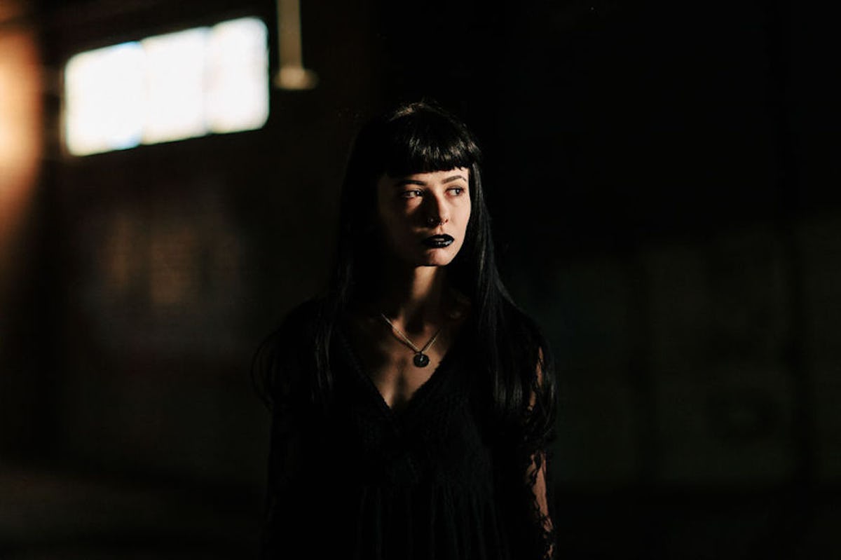 A woman dressed like a vampire for Halloween stands in shadows with sunlight in her face.