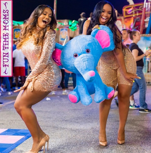 Two Black women pose at a carnival holding a blue stuffed elephant. 