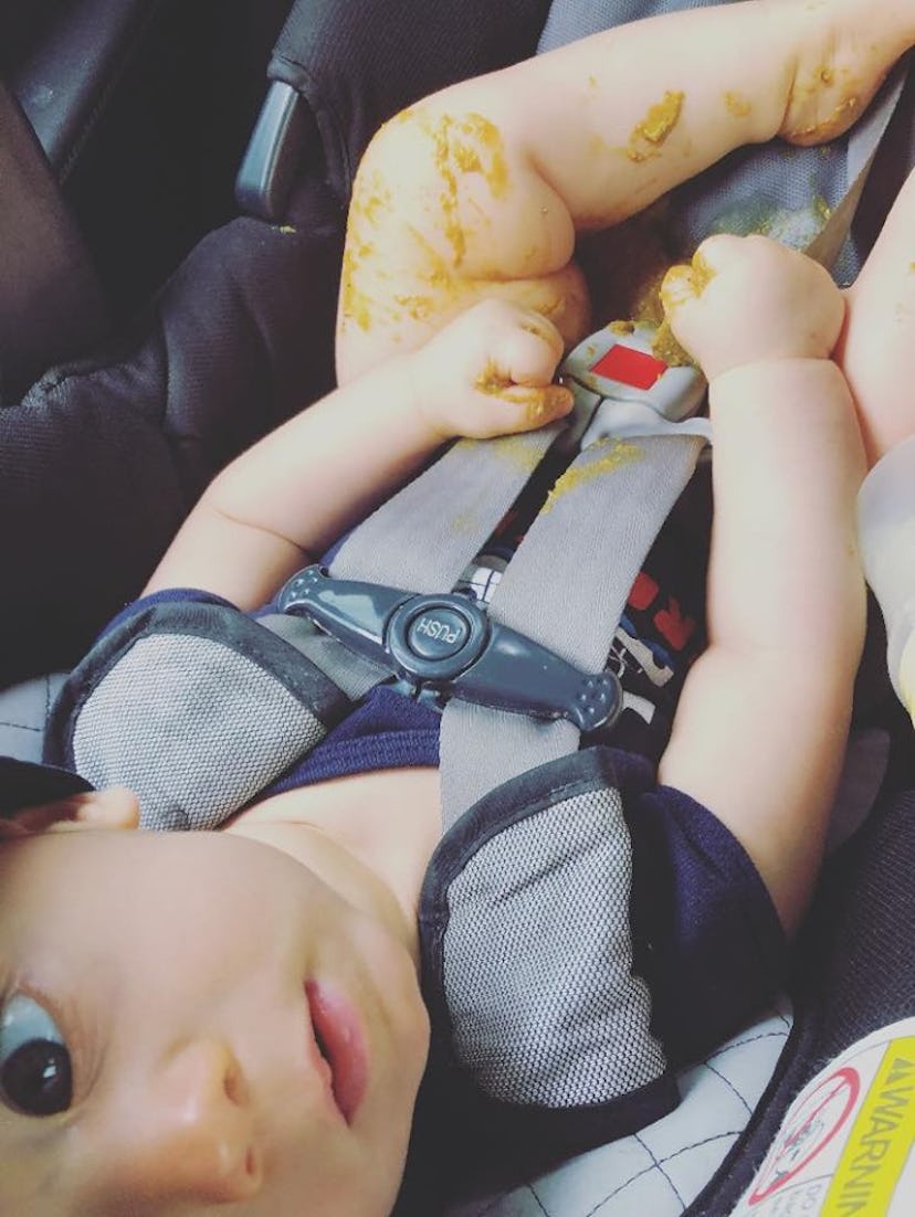A 9-month-old baby sitting in his car seat, looking up at the camera and playing with his poop after...