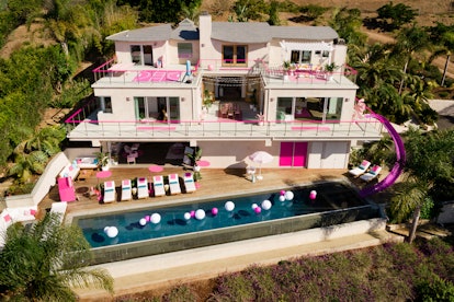The exterior of Barbie's Malibu Dreamhouse during the day features an infinity pool, pink and white ...