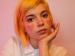 A teenage girl with short dyed hair and hearts painted on her cheeks looks like an e-girl.