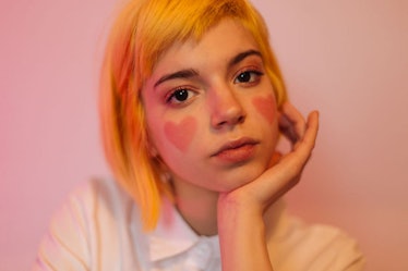 A teenage girl with short dyed hair and hearts painted on her cheeks looks like an e-girl.