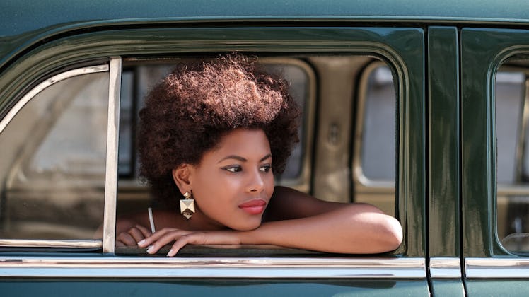 Woman smiles wearing earrings and looks out of the window of a vintage car.