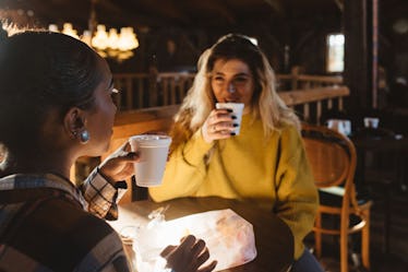 Two friends drink apple cider and chat at a cider mill in the fall.