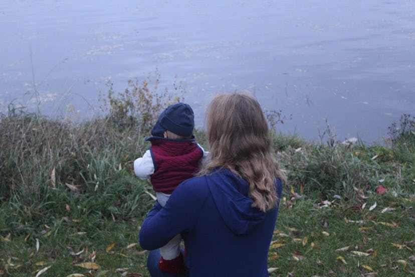 An author holding her young son, sitting by the side of a lagoon.