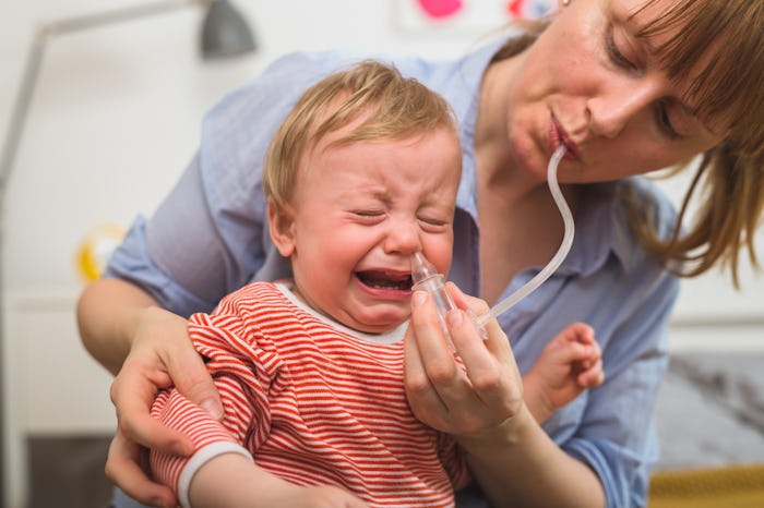 A toddler sitting on his mom's lap crying as his nose is suctioned