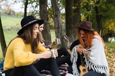 A group of friends laugh and drink tea during a fall picnic.
