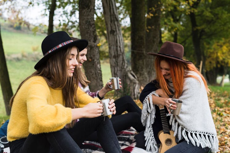 A group of friends laugh and drink tea during a fall picnic.