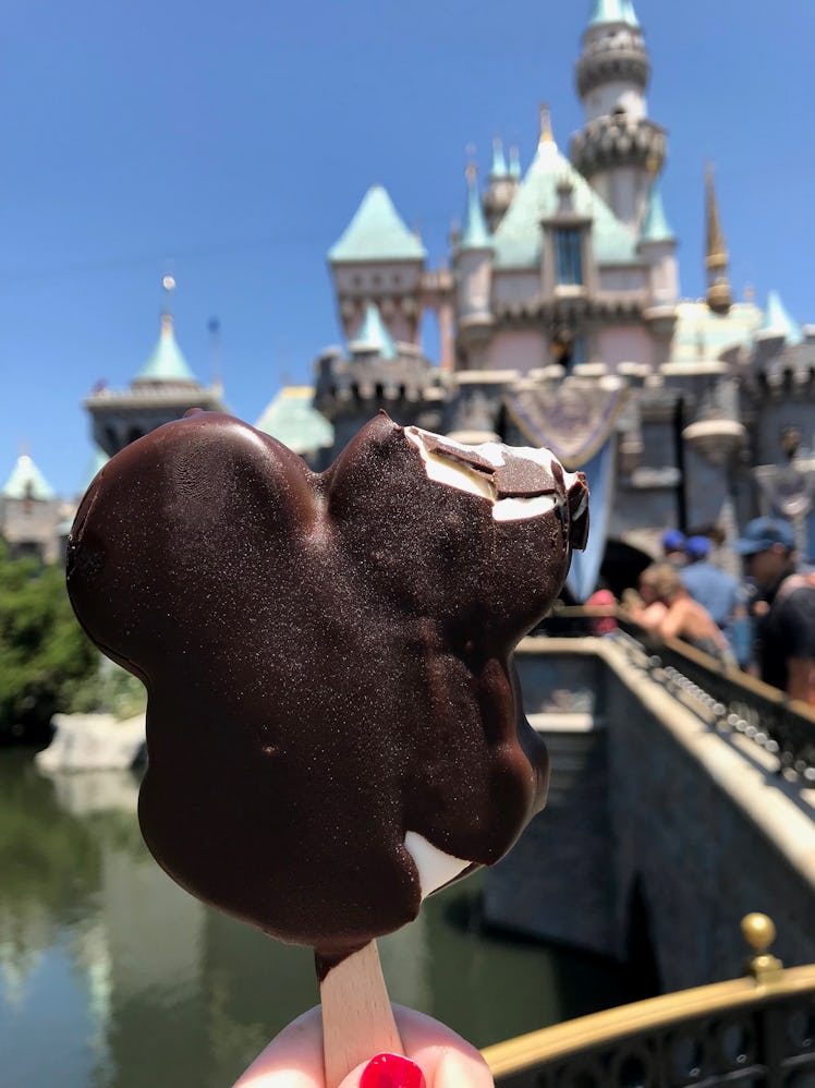 A Mickey-shaped ice cream bar being held up in front of the castle in Disneyland. 