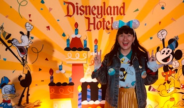 A woman wearing sequinned Minnie ears stands in front of a birthday Disneyland Hotel sign at Disney....