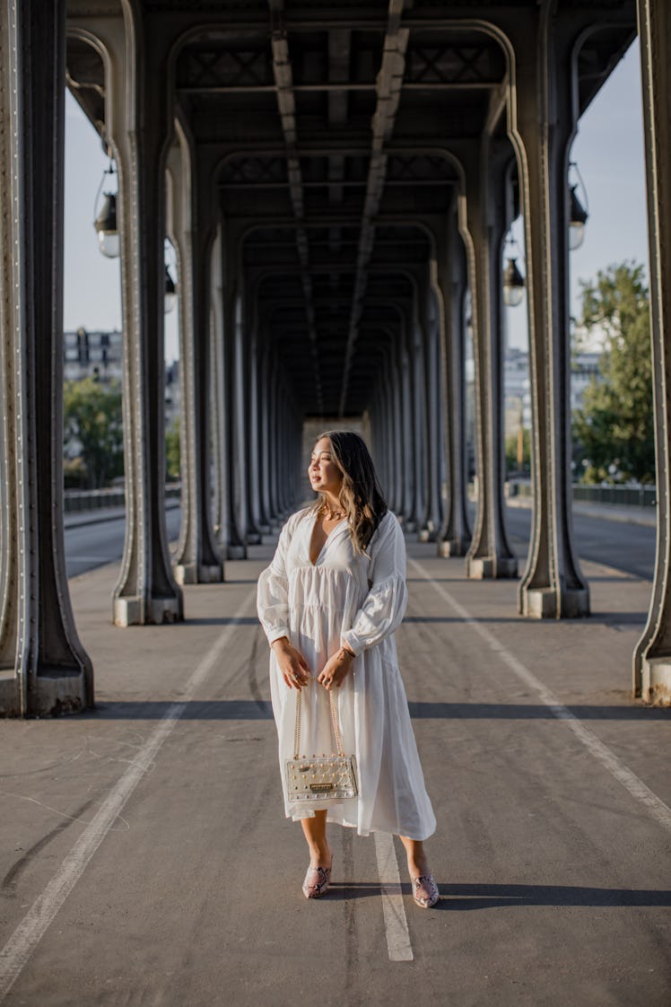 A woman in white long-sleeved dress and pink shoes stands at the center of the BIr-Hakeim bridge in ...
