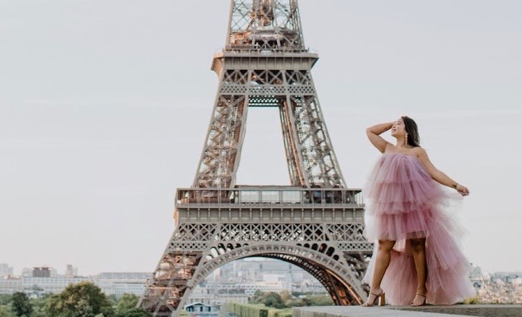A girl dressed in a pink tulle dress smiles and poses in front of the Eiffel Tower in Paris.