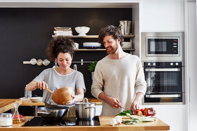 A happy couple cooks in their kitchen together.