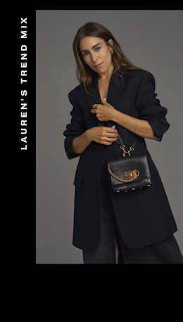 A woman posing in a black coat, pants and a leather purse with golden details