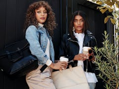 Two girls stand in front of a black fence with coffee cups and bags from Shay Mitchell's BÉIS winter...