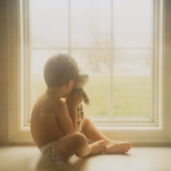 Boy holds teddybear in window