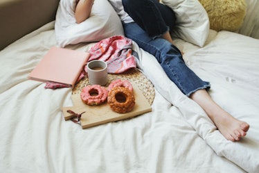 A girl lays in a comfy bed with a plate of pumpkin doughnuts, a mug of coffee, and a pink notebook.
