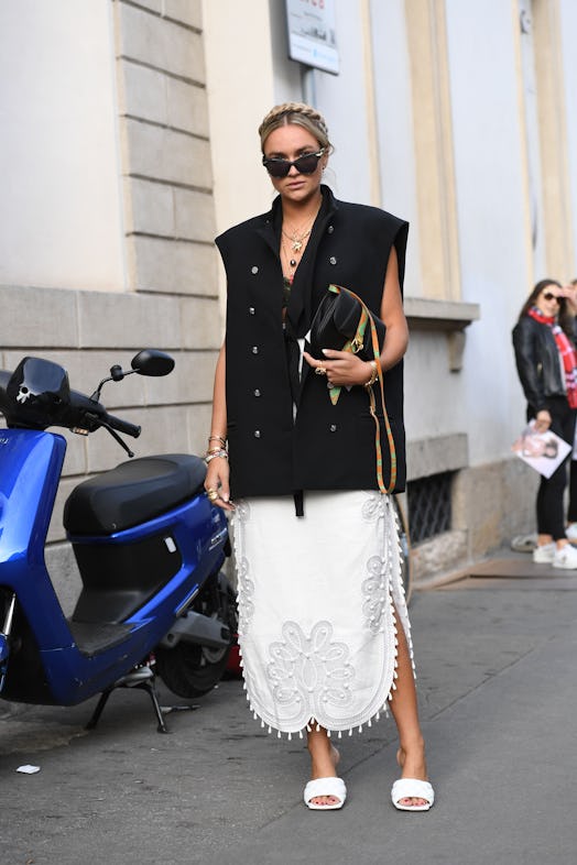 Street style photo of a woman wearing a boxy, oversized vest and white lace dress with Bottega Venet...