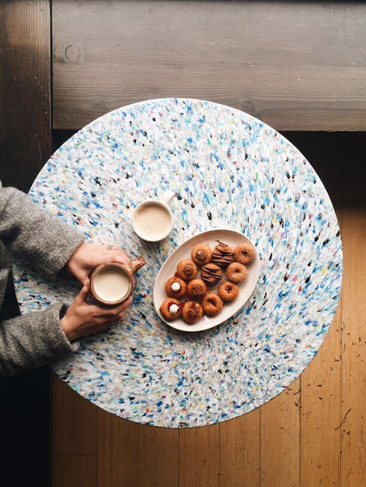 A woman sits at a multicolor table with a plate of pumpkin doughnuts and lattes.