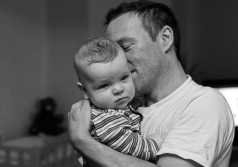 A father holds their baby. Equitable parental leave may help the motherhood wage penalty over time, ...