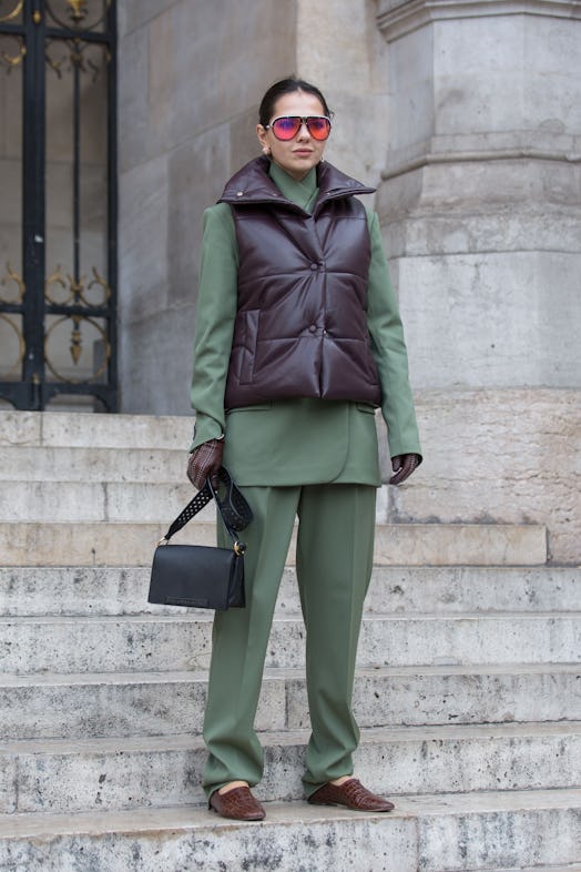 Street style photo of a woman wearing a puffer vest over a sleek green suit at Fashion Week. 