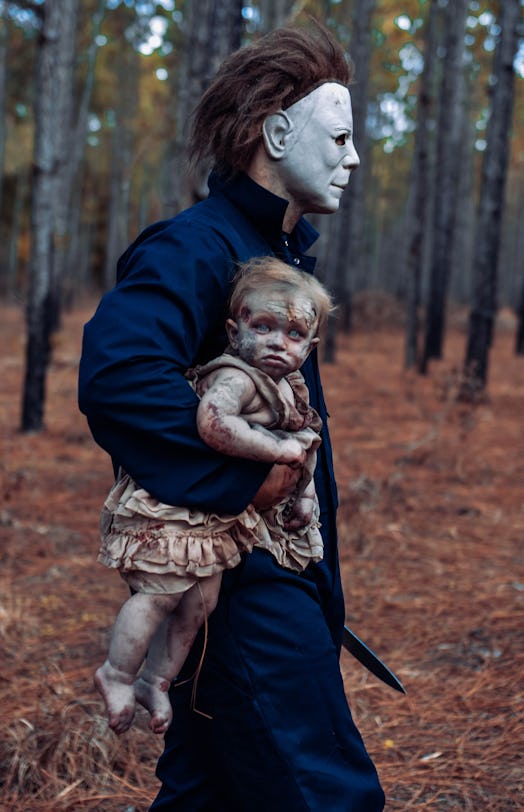 A dad dressed as Michael Myers carries his zombie baby away.