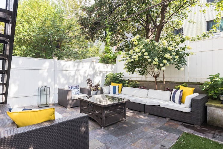 An outdoor patio features black wicker furniture that's topped with white cushions, accented with so...
