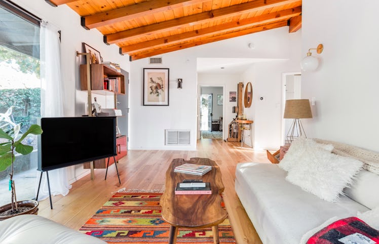 A spacious living room with hardwood floors and vented ceilings, a white couch with fluffy white pil...