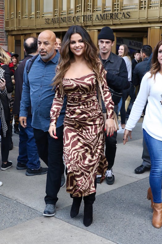 Selena Gomez in a brown-beige sating long-sleeved dress with wavy stripes and black boots