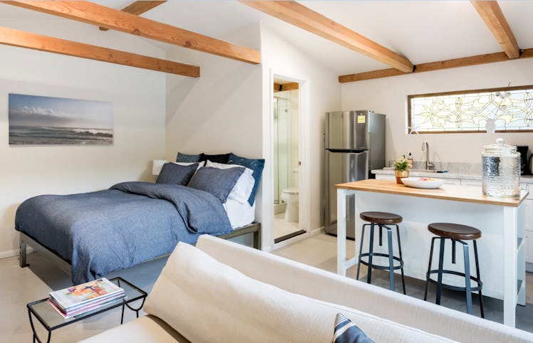 An open floor plan studio apartment in LA on Airbnb showcases a queen bed, a counter with two stools...