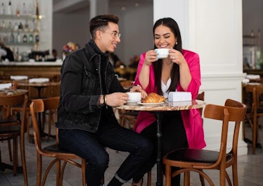 A young couple enjoys coffee and croissants at a small bistro-like table in an empty restaurant. 