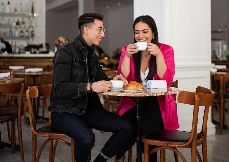 A young couple enjoys coffee and croissants at a small bistro-like table in an empty restaurant.