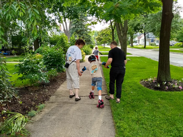 A grandmother helps her grandchildren learn to roller skate.