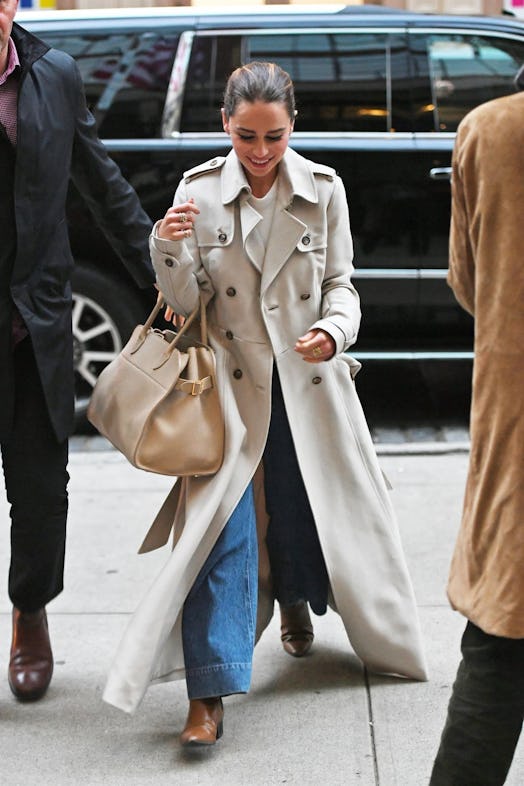 Emilia Clarke in a light trench coat, jeans and a beige bag 