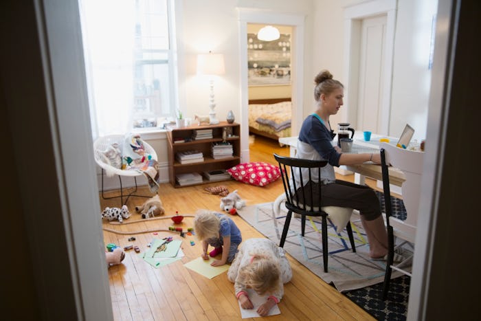 woman working on laptop as two children play on floor