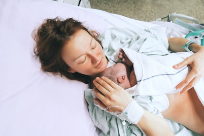 mother holding newborn child in hospital bed with her eyes closed