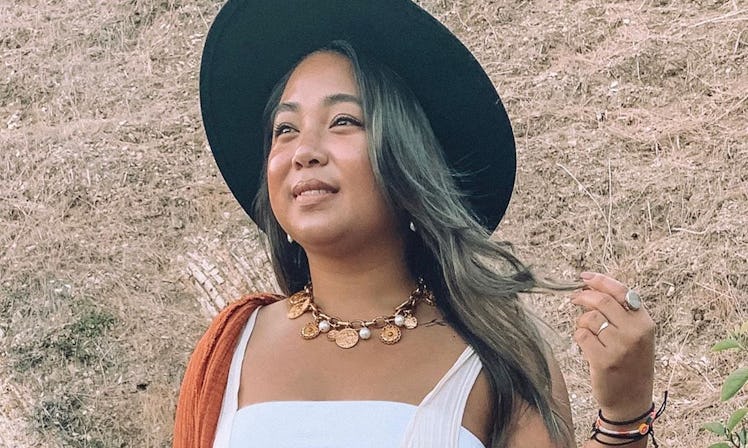 A woman wearing a black felt hat looks off into the distance holding a strand of her hair.