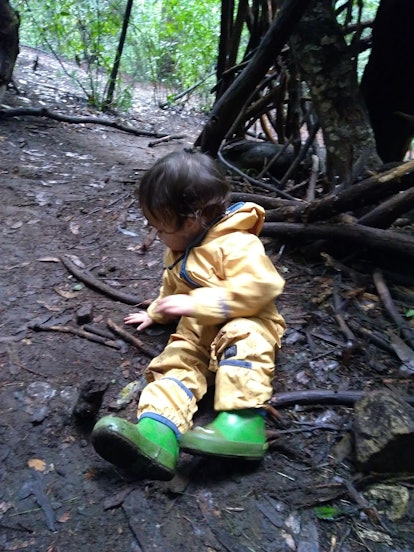 A picture of a young child in a rain coat, playing in the forest. 