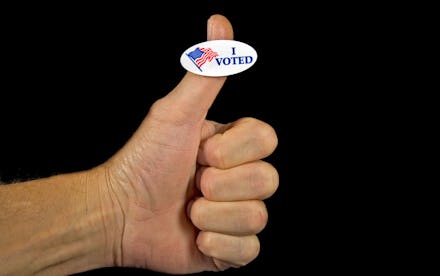 A thumb up in front of a black background and 'I voted' sticker on it