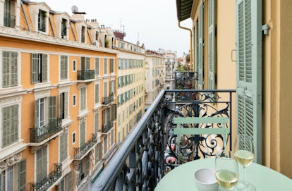 A balcony in Nice has a teal table and chairs set and overlooks orange and yellow buildings.