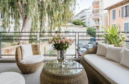A luxe apartment in Cannes has a balcony with plush white couches, roses, and lots of greenery.
