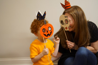 A mother and child with Halloween masks of a carved pumpkin and skull 